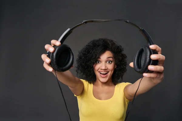 Smiling woman giving you headphones, studio shot — Stock Photo, Image