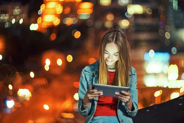 Chica en la noche paisaje urbano de fondo con luces de calle, utilizando una tableta digital — Foto de Stock