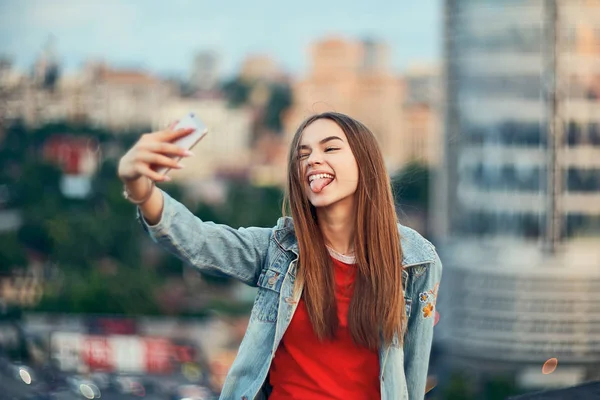 Девушка-подросток на фоне городского пейзажа делает автопортрет со своим смартфоном — стоковое фото