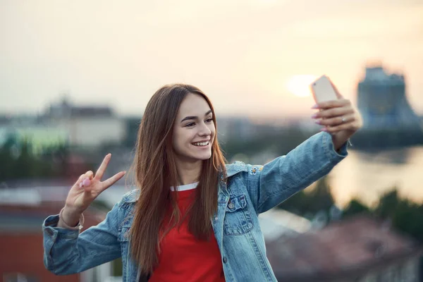 Chica adolescente en el fondo del paisaje urbano haciendo autorretrato con su teléfono inteligente — Foto de Stock