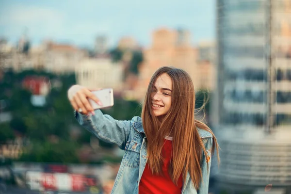 Nastolatka na tle miejskiego krajobrazu robi autoportret ze swoim smartfonem — Zdjęcie stockowe