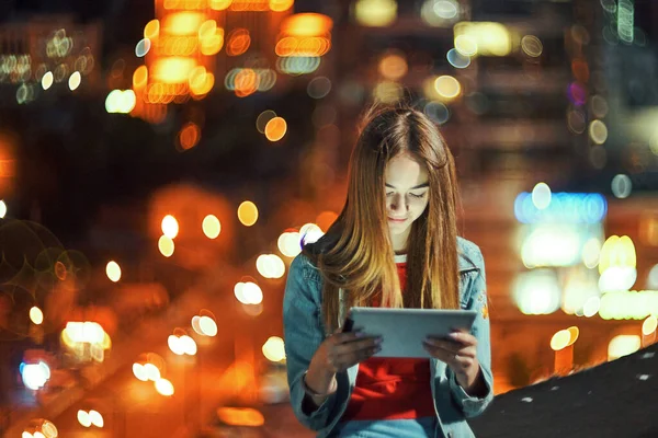 Chica en la noche paisaje urbano de fondo con luces de calle, utilizando una tableta digital — Foto de Stock