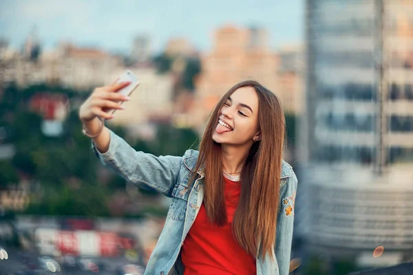 Chica adolescente en el fondo del paisaje urbano haciendo autorretrato con su teléfono inteligente — Foto de Stock