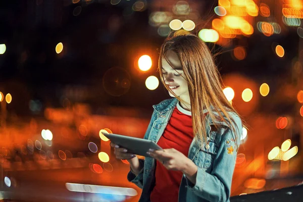 Girl on night cityscape background with street lights, using a digital tablet — Stock Photo, Image