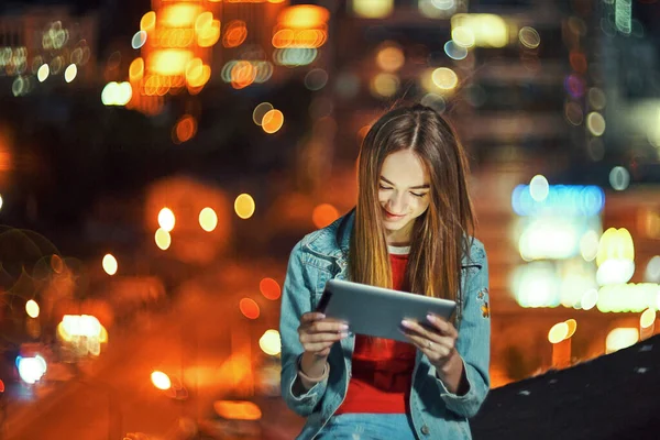 街路灯と夜の街並みの背景に素敵なティーンの女の子 デジタルタブレットを使用して — ストック写真
