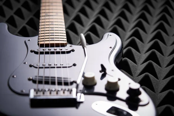 Black electric guitar lying on acoustic foam panel — Stock Photo, Image