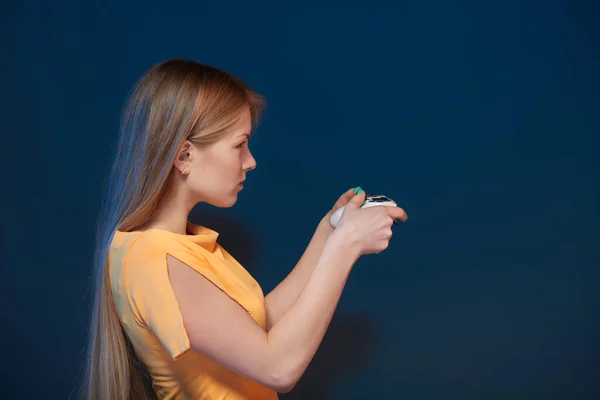 Profil seorang gadis bermain video game dengan joystick di latar belakang biru — Stok Foto
