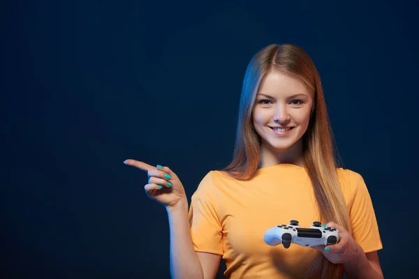 游戏女孩 快乐的女孩拿着电子游戏的操纵杆 指指点点旁边空白的复制空间 蓝色背景 — 图库照片
