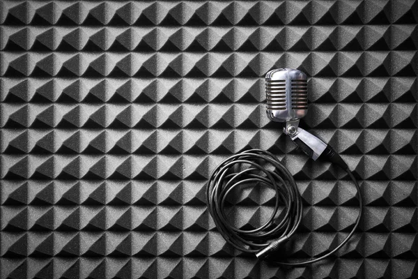 Retro microphone with cable lying on acoustic foam panel background, flat lay