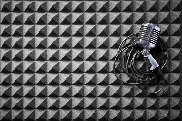 Retro microphone with cable lying on acoustic foam panel background, flat lay