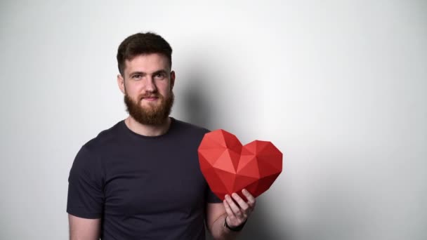 Poloviční portrét mladého vousatého hipsterského muže držícího červený tvar srdce — Stock video