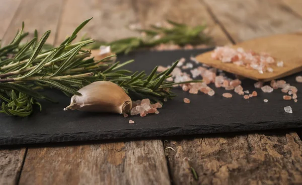 Salt, peppar, vitlök och rosmarin på en skärbräda — Stockfoto