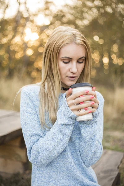 Autumn woman drinking coffee. Fall concept of young woman enjoying hot drink from disposable coffee cup in fall landscape.