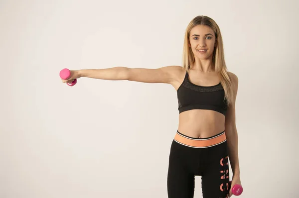 Joven deporte sexy fitness rubia posando en la pared blanca en una camiseta sin mangas y polainas, zapatillas de deporte —  Fotos de Stock