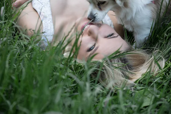 Bionda dagli occhi azzurri sdraiata sull'erba con i denti di leone. Carino giovane fidanzata bella ridendo in caldo giorno soleggiato — Foto Stock
