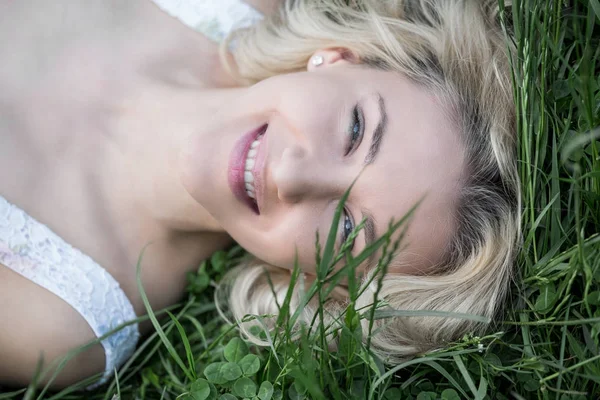 Modrooký blondýna ležící na trávě s pampelišky. Roztomilý mladý Girfriend krásný smích v teplý slunečný den — Stock fotografie
