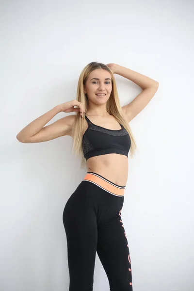 Junge Sport sexy Fitness blonde Frau posiert auf weißer Wand in einem Tank-Top und Leggings, Turnschuhe — Stockfoto