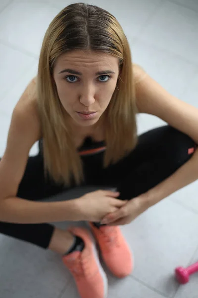 Joven deporte sexy fitness rubia posando en la pared blanca en una camiseta sin mangas y polainas, zapatillas de deporte —  Fotos de Stock