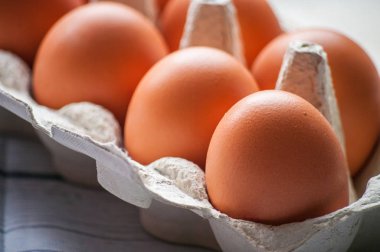 Beyaz ahşap arka planda yumurta kutusundaki çiğ tavuk yumurtalarının yakın plan görüntüsü