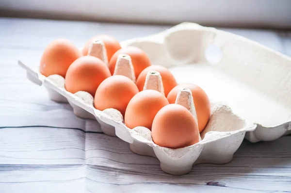 Beyaz ahşap arka planda yumurta kutusundaki çiğ tavuk yumurtalarının yakın plan görüntüsü