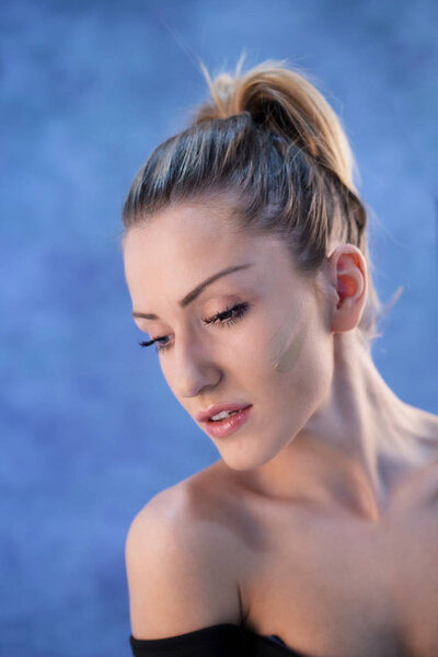 Красивая молодая блондинка с хвостиком, позирующая в студии перед синей стеной
