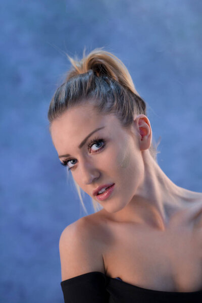 Красивая молодая блондинка с хвостиком, позирующая в студии перед синей стеной
