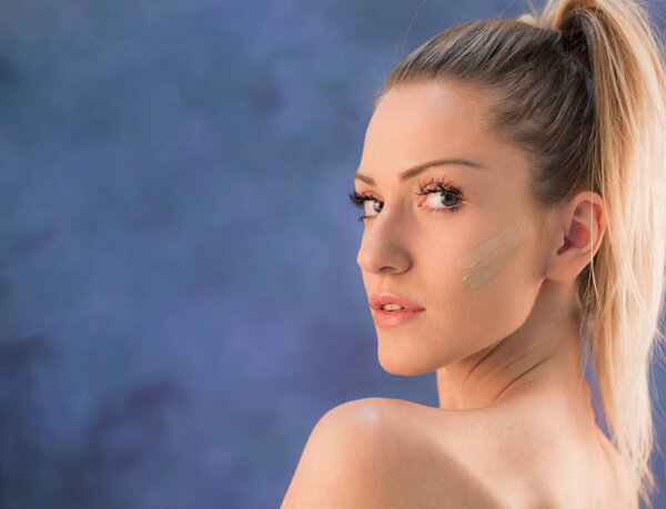 Красивая молодая блондинка с хвостиком, позирующая в студии перед синей стеной
