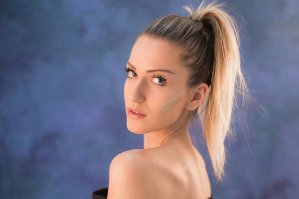 Красивая молодая блондинка с хвостиком, позирующая в студии перед синей стеной
