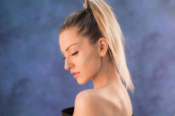 Красивая молодая блондинка с хвостиком, позирующая в студии перед синей стеной
