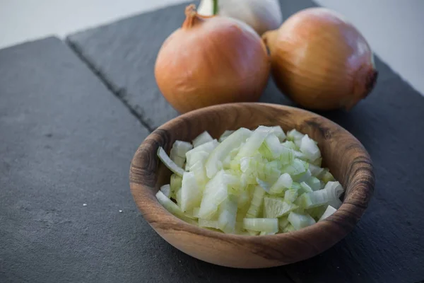 chopped fresh and raw white onion slices in wooden bowl with bulbs