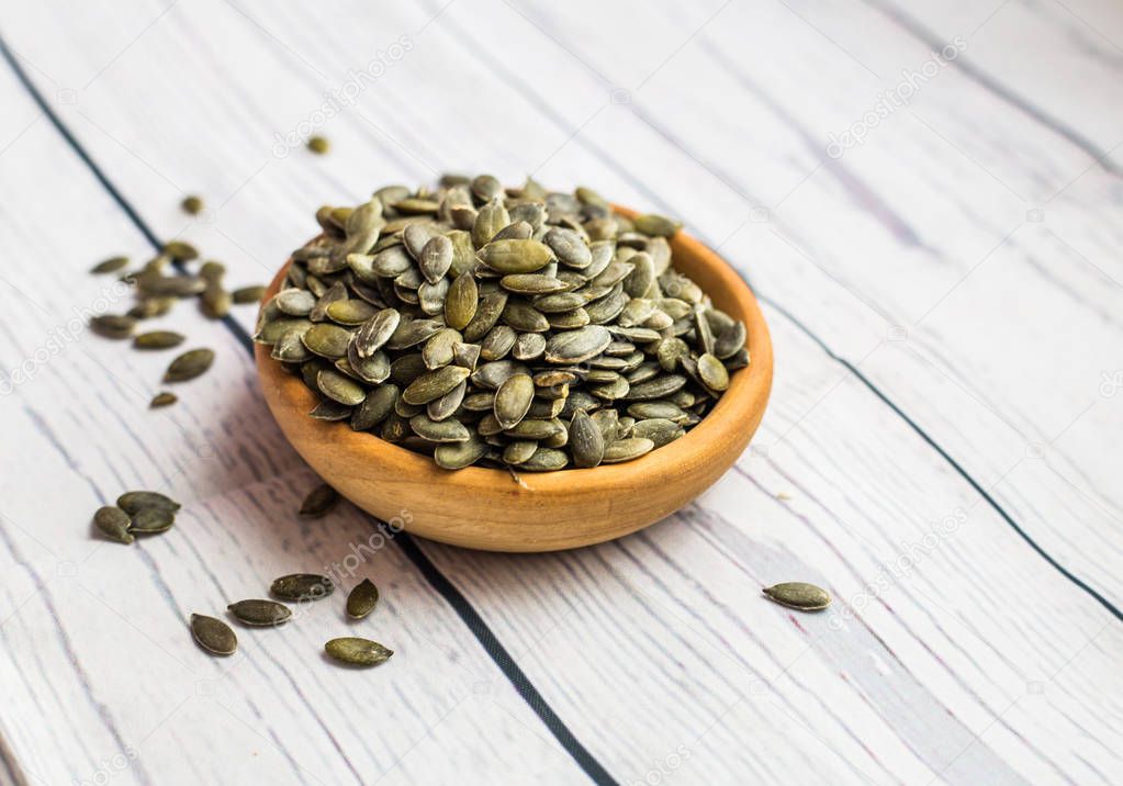 bowl with raw pumpkin seeds on wooden background