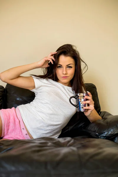 コーヒー カップ手に泡自宅にソファに横になっている白い シャツの魅力的な女性 — ストック写真