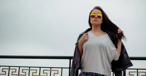 时尚的年轻女子在太阳镜下的皮革夹克在城市背景 — 图库照片