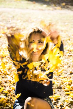 Sonbahar sezonu. Mavi kazaklı bir kadının portresi yapraklarla oynuyor.