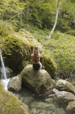 Siyah mayo giyen seksi sarışın kadın doğada poz veriyor.