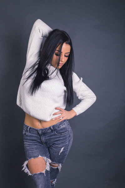 beautiful model posing in jeans and sweater against gray 