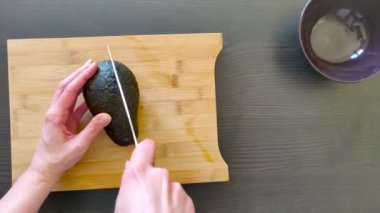 Yakın çekim, bıçakla iki dilimde avokado kesen eller.