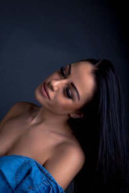 Çekici esmer kadın kameraya mavi gömlekli poz veriyor.