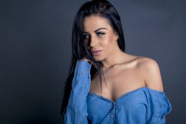 Çekici esmer kadın kameraya mavi gömlekli poz veriyor.