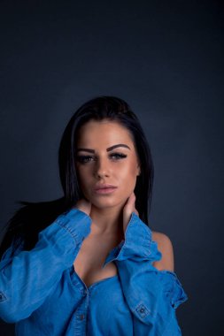 Çekici esmer kadın kameraya mavi gömlekli poz veriyor.