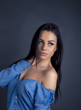 Çekici esmer kadın kameraya mavi gömlekli poz veriyor.