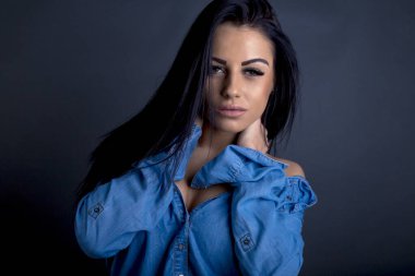 Çekici esmer kadın kameraya mavi gömlekli poz veriyor.