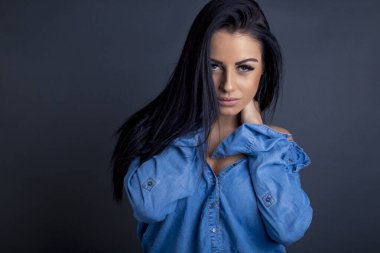 Çekici esmer kadın kameraya mavi gömlekli poz veriyor.