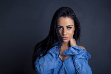 Çekici esmer kadın kameraya mavi gömlekli poz veriyor.