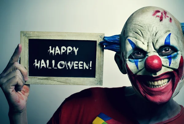 Kwade clown met een bord met de tekst vrolijke Halloween — Stockfoto