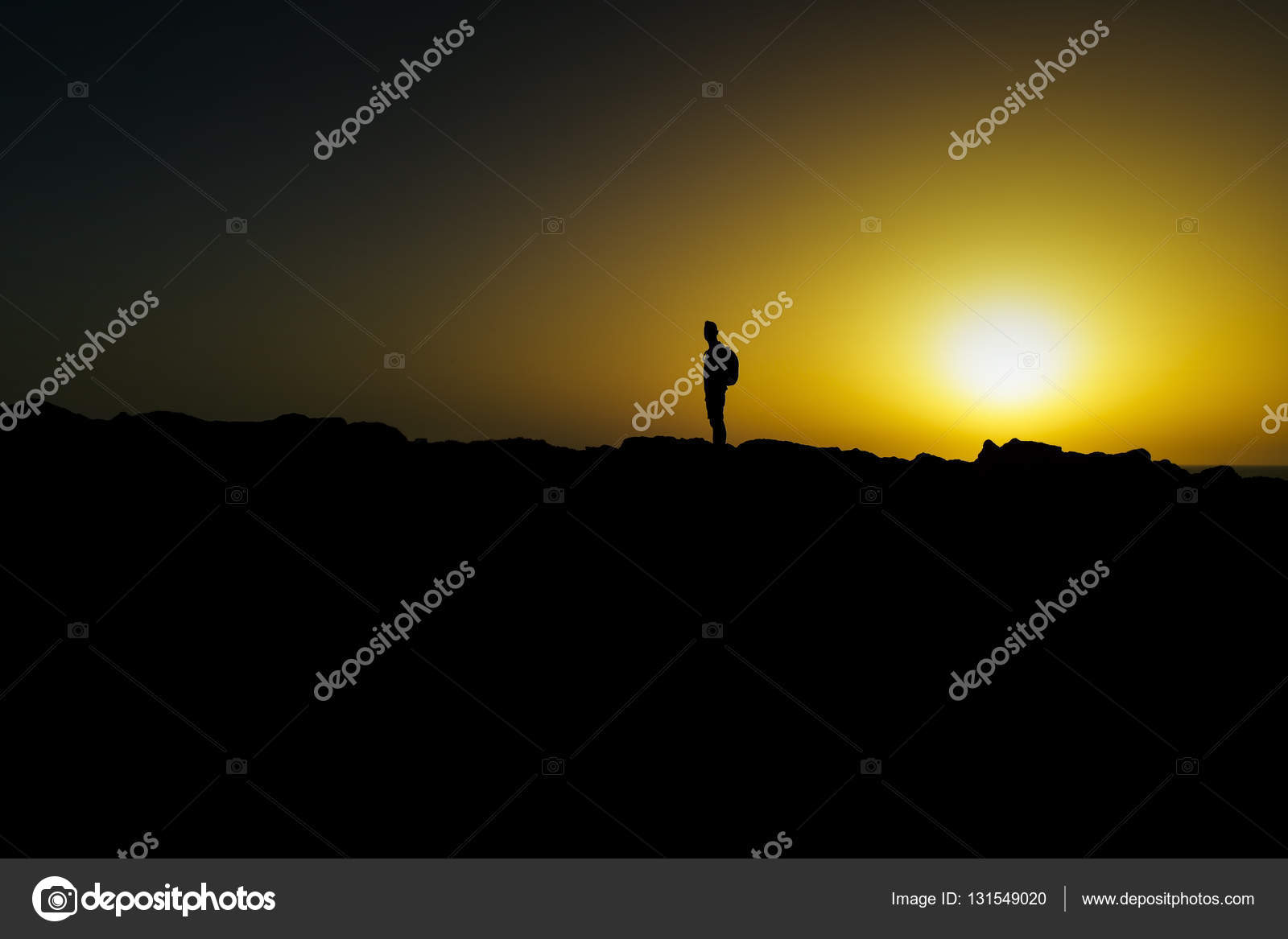 La silhouette di un giovane uomo indoeuropeo portando uno zaino alla schiena al crepuscolo contro un cielo colorato di giallo con l orizzonte e il sole