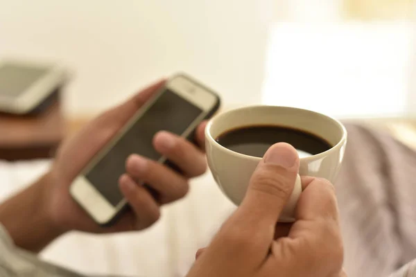 Ung man med en kopp kaffe med en smartphone — Stockfoto