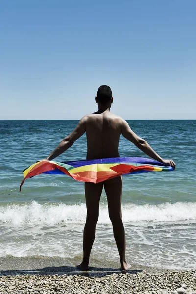 Hombre con una bandera de arco iris en la playa — Foto de Stock