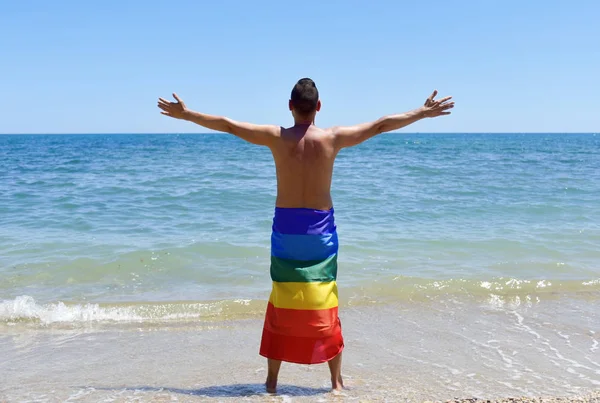 Man med en regnbågsflaggan framför havet — Stockfoto