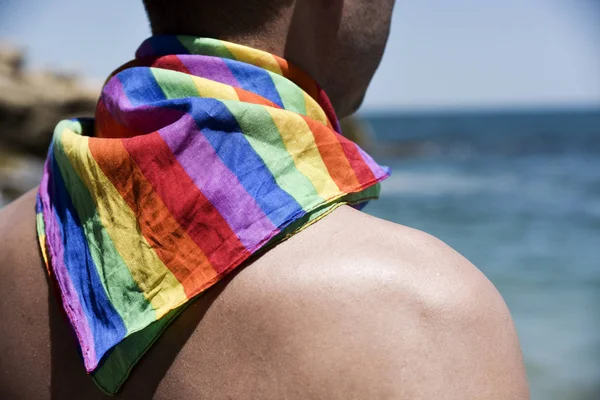 Hombre con una bandera de arco iris frente al océano —  Fotos de Stock
